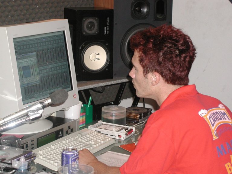 Ein Bandmitglied arbeitet am Studiocomputer zwischen Monitoren und Mischtechnik.