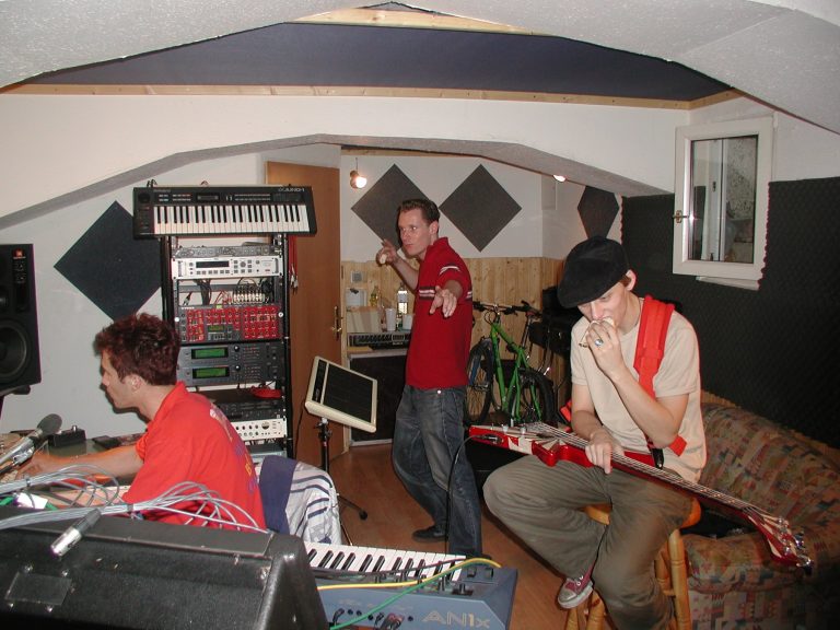 Bandmitglieder arbeiten gemeinsam zwischen Studiocomputer, Keyboards und Racktechnik.