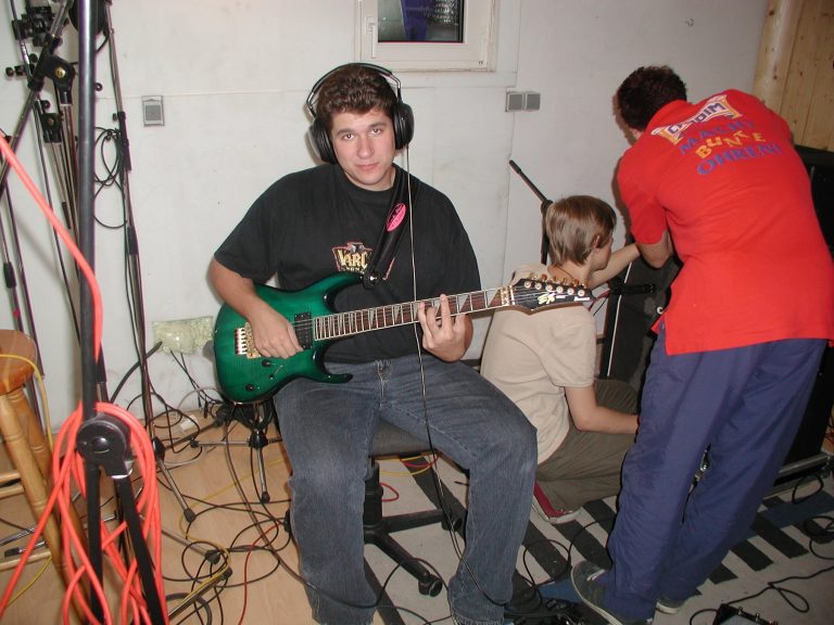 Alexander Pfeiffer spielt im Studio eine grüne E-Gitarre, während im Hintergrund an der Technik gearbeitet wird.