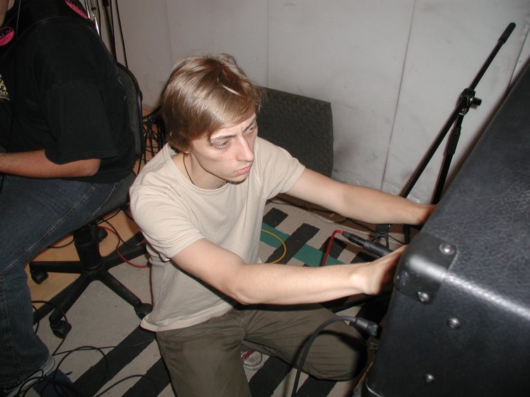 Ein Bandmitglied justiert kniend das Equipment im Aufnahmeraum.