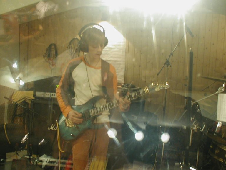Michael Trimmel spielt hinter der Studioscheibe eine E-Gitarre ein.