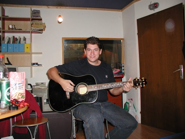 Ein Bandmitglied spielt zwischen Studiotechnik und Instrumentenkoffern Akustikgitarre.